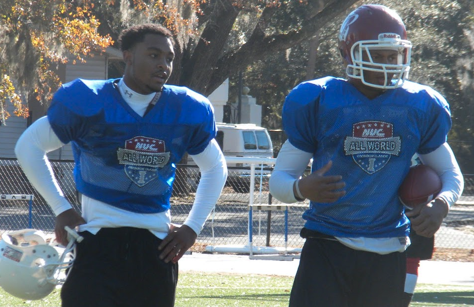 Two NUC All World players in blue practice jerseys standing together on the field