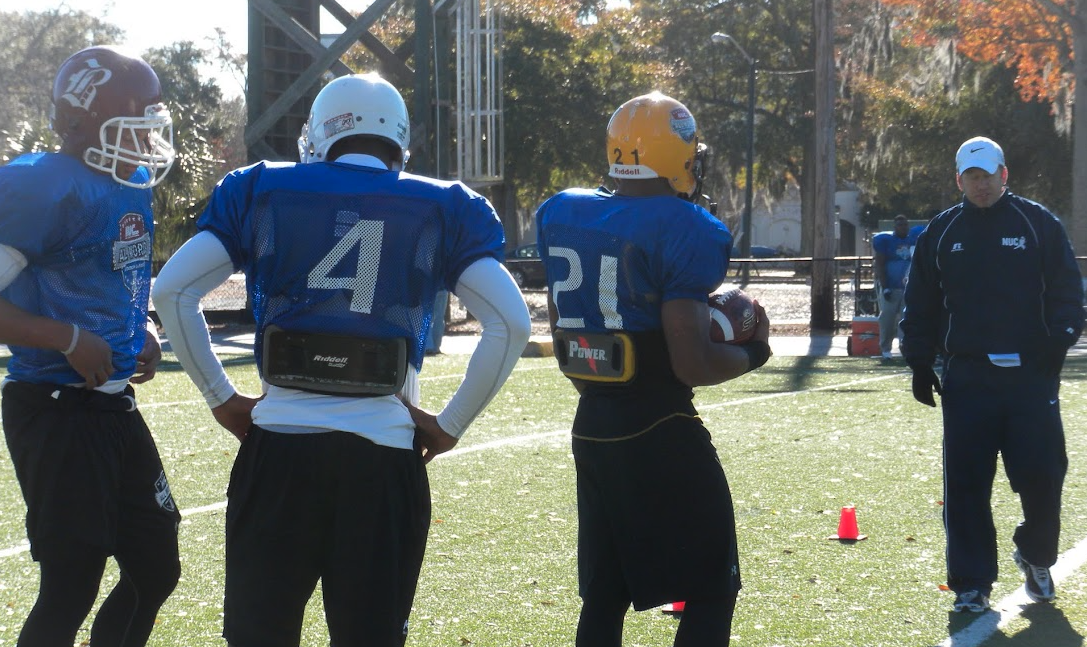 NUC All World players in blue practice jerseys listening during field instruction