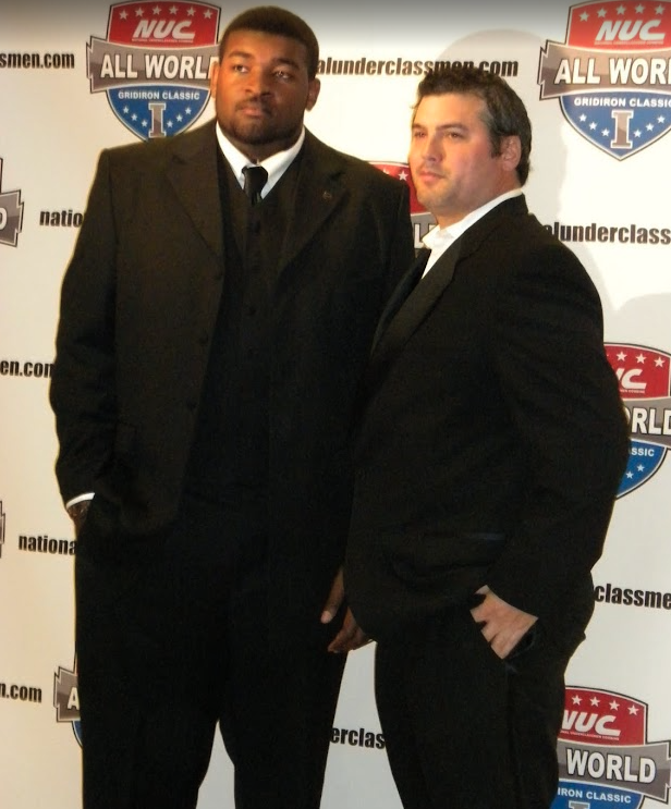 Two NUC All World players posing in suits in front of the event backdrop