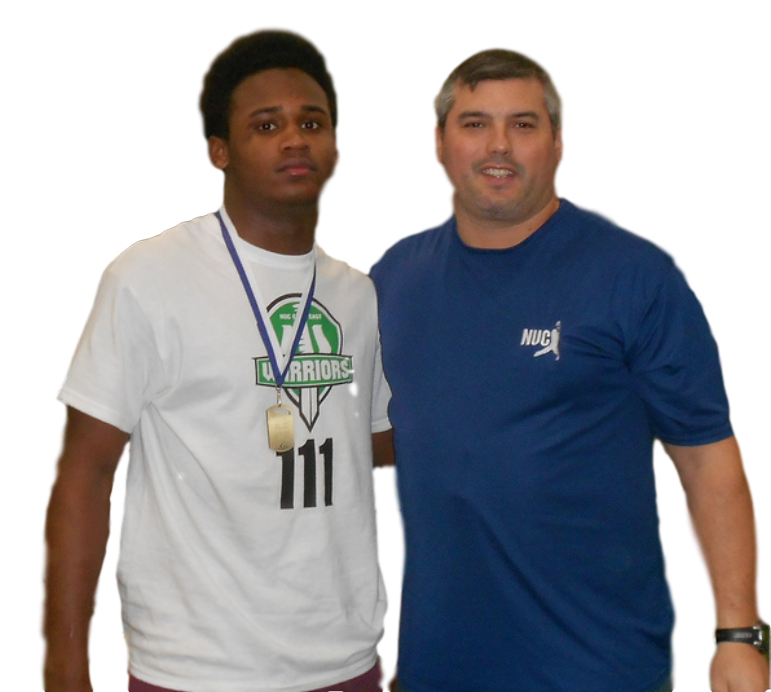 Coach David Schuman in a one-on-one conversation with a high school football prospect wearing a black NUC Warriors jersey after a combine 40-yard dash, reviewing his testing numbers.